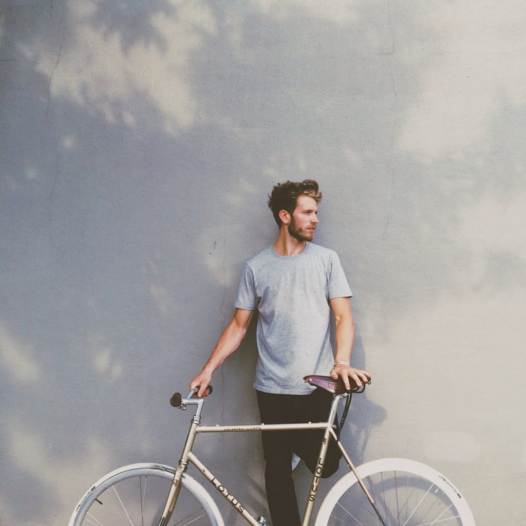 Mies nojaa seinään pidellen valkearenkaista polkupyörää pystyssä aurinkoisessa säässä.