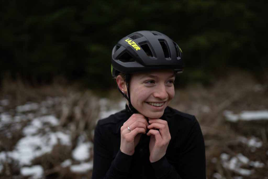 Nuori nainen valitsemassa pyöräilykypärää keväisessä suomalaisessa maalaismaisemassa.
